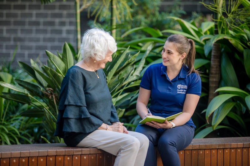 Senior client and allied health professional sitting on a bench, conversing
