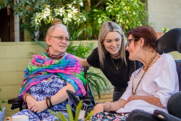 Staff member talking and smiling with two people in wheelchairs