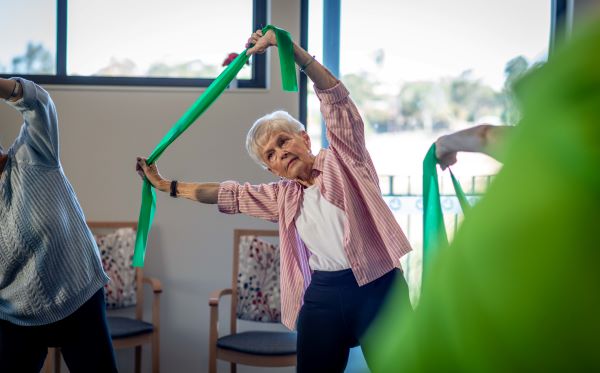 Lady exercising in group class, holding theraband over her head and leaning to the side