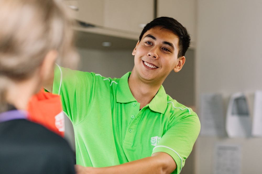 Man wearing Wesley Mission Queensland shirt smiles as he hands over a red grocery bag